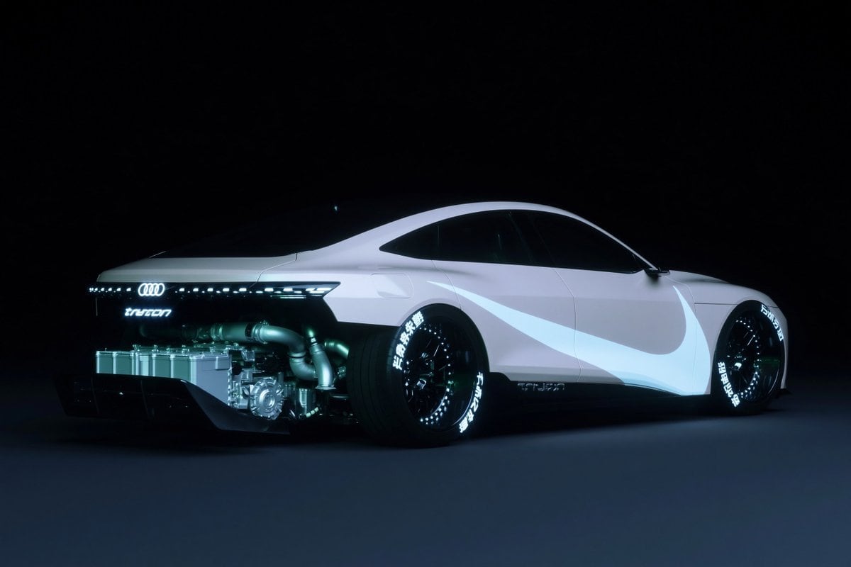 A futuristic concept coupe based on an Audi, shown in a low rear three-quarter side view facing right, isolated in a vast black studio with a dark matte floor and almost no background det...