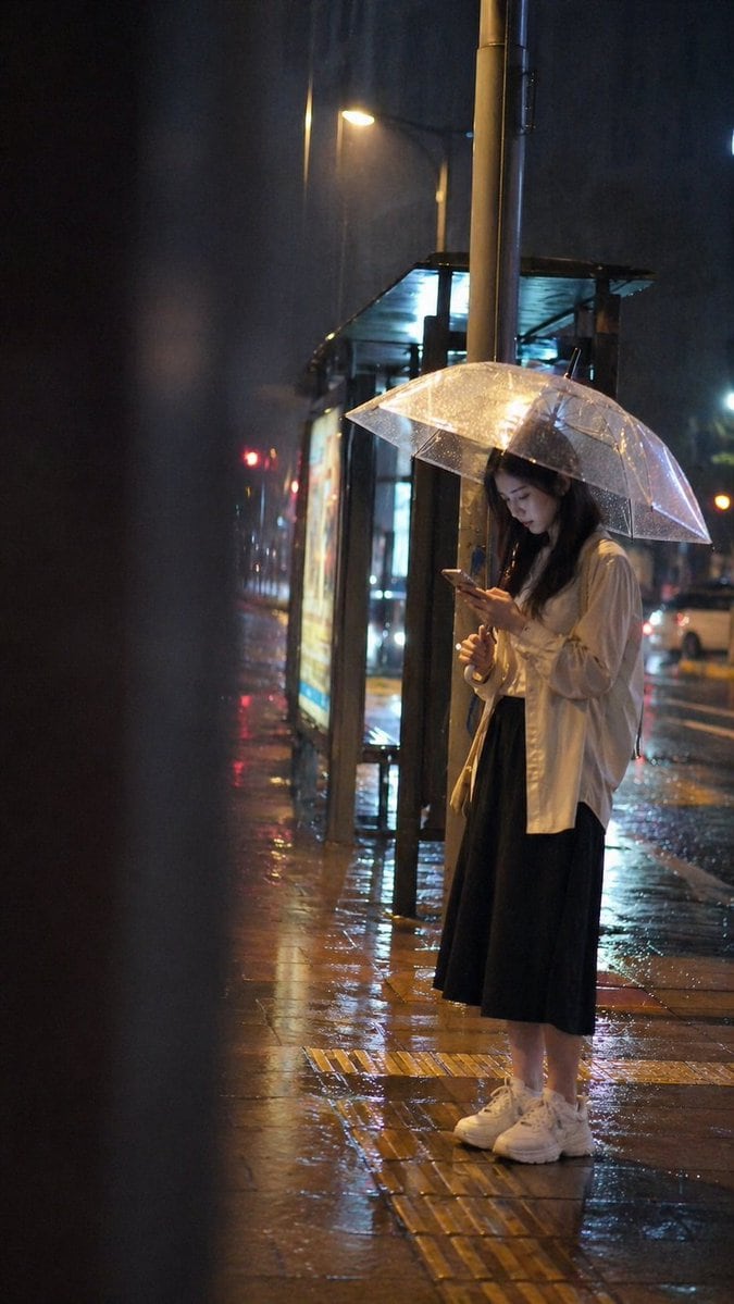 一个高度细致、氛围感十足的提示词，用于生成雨夜公交车站人物的真实抓拍快照。