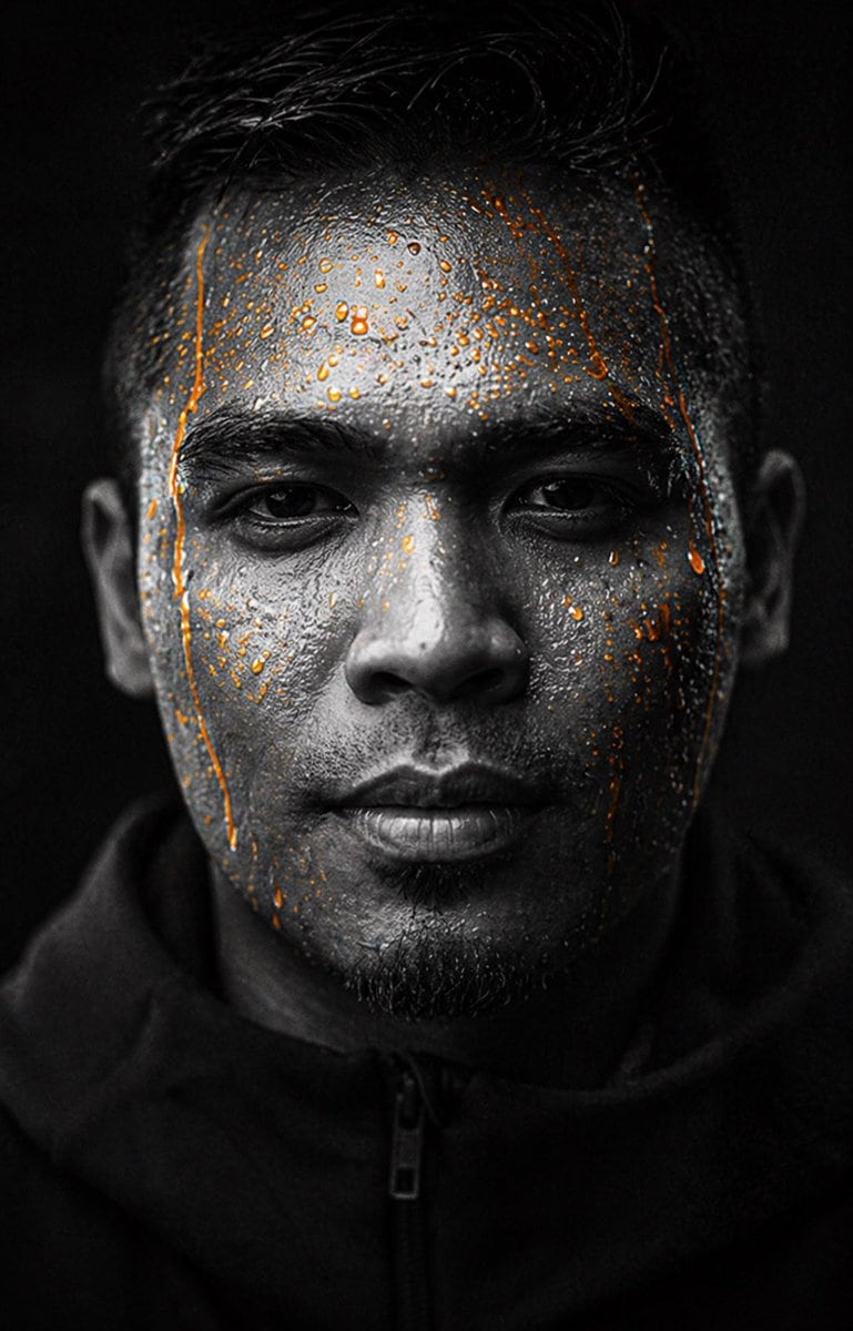 A dramatic, high-contrast studio portrait of a male athlete or model in the visual style of a premium sports drink advertisement, centered and facing straight toward the camera in a tight...