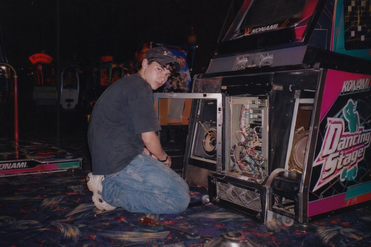 Generates a nostalgic, flash-lit photograph of someone repairing an open arcade cabinet in a dimly lit gaming center.