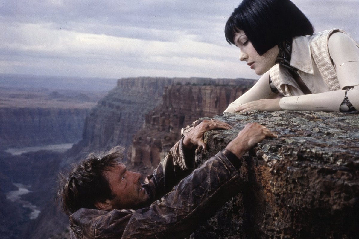 A cinematic still from a 1990s American sci-fi action movie. A rugged male protagonist with a dirty face and a distressed brown leather jacket is desperately dangling from the edge of a r...