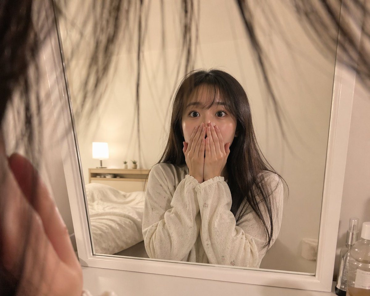 A realistic first-person perspective photo in a softly lit minimalist bedroom at night, as if the viewer is standing very close to a standing mirror and looking at their own reflection. I...