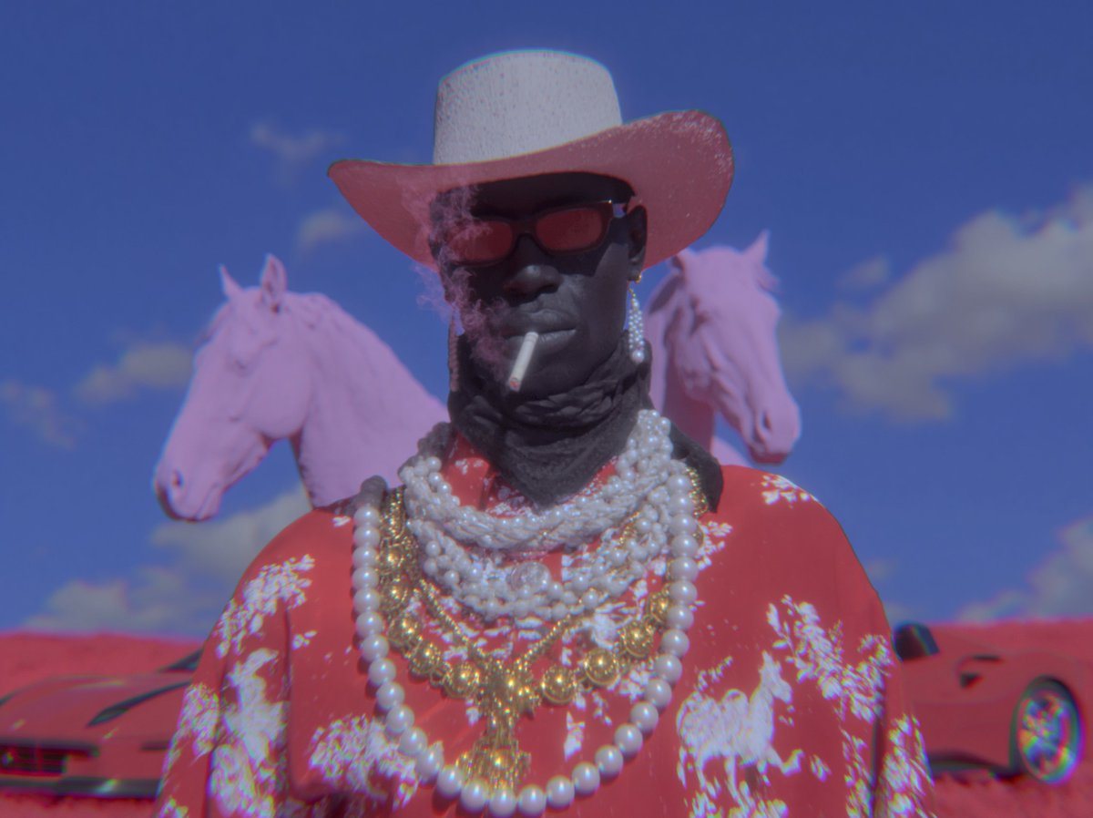 A surreal fashion portrait of a mysterious cowboy figure centered in the frame, shot from the chest up against a vivid cobalt-blue daytime sky with a few soft white clouds. The person’s f...