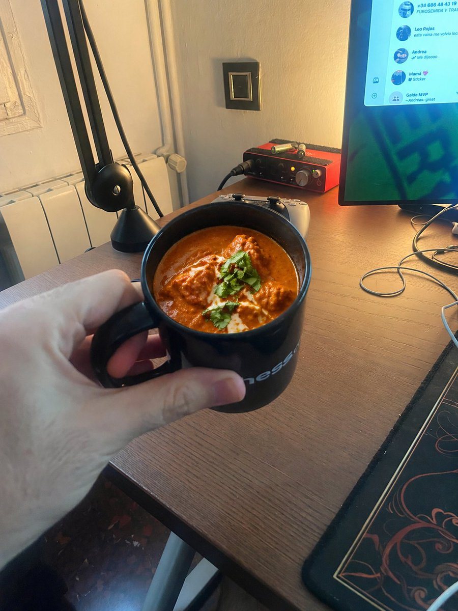 A photorealistic joke snapshot of a hand holding a black mug filled with chicken tikka masala in a warm-lit desk setup, ideal for surreal social media humor images.