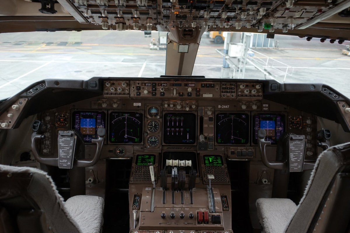 Ultra-realistic interior photograph of a Boeing 747 cockpit viewed from slightly behind and between the two pilot seats, centered and perfectly symmetrical, showing the full main instrume...