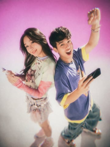 A studio portrait of two young East Asian adults standing back-to-back against a bright pink to white gradient backdrop. The photo features a Y2K nostalgic 90s teen magazine aesthetic wit...